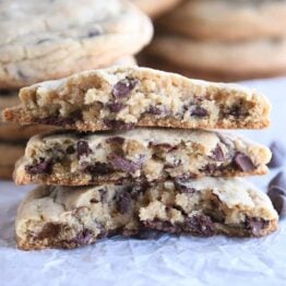 three half chocolate chip cookies stacked on each other on white parchment paper