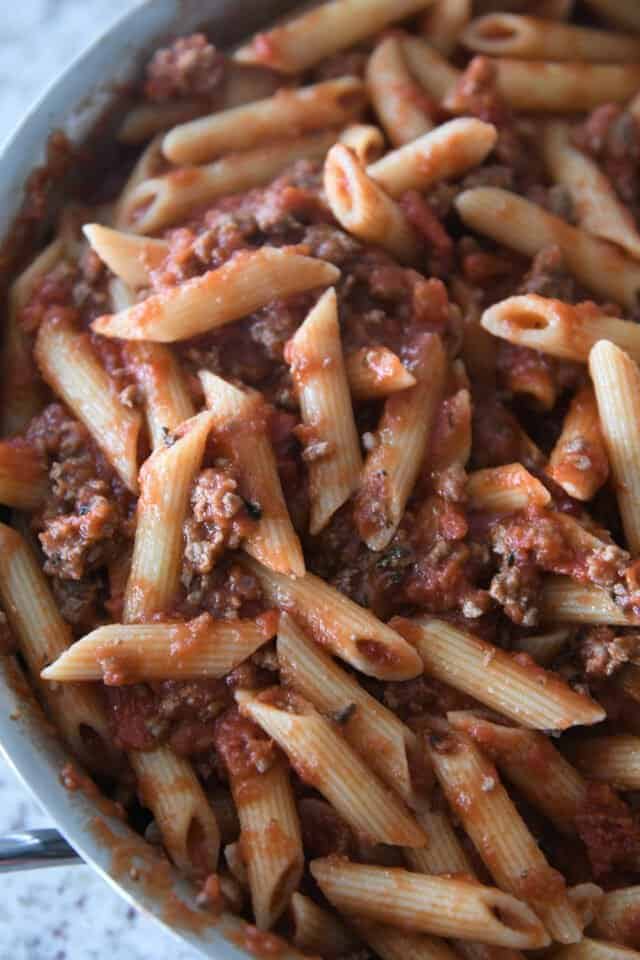 Penne noodles in pan with red sauce and ground beef.