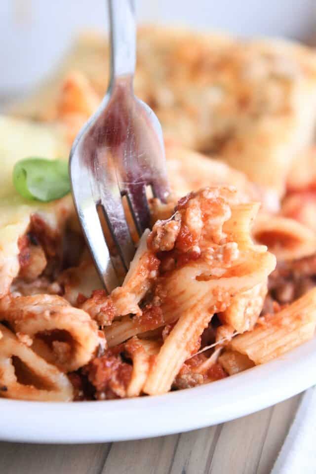 Fork taking a bite of penne noodles with red sauce on white plate.