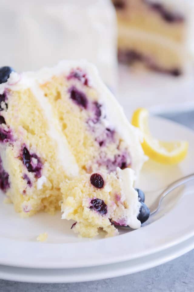 Slice of lemon blueberry cake on white plate with bite on fork.