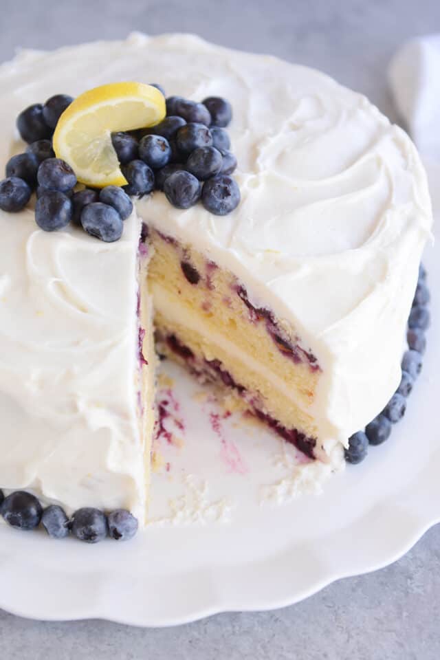 Two layer lemon blueberry cake with whipped lemon frosting and lemon and blueberries on top for garnish.