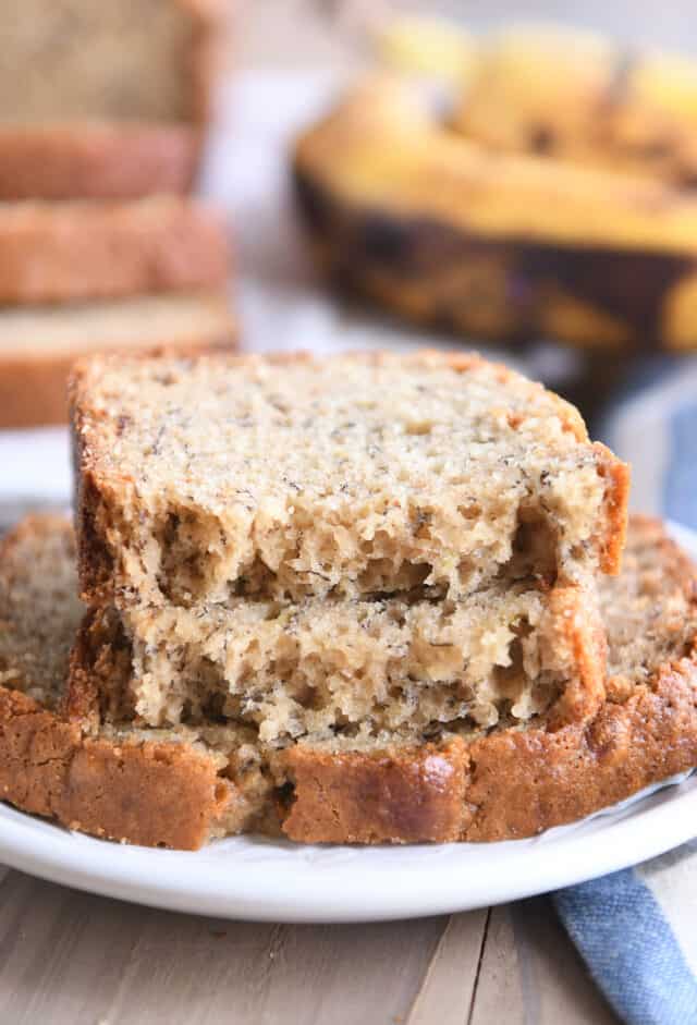 Two halves of banana bread stacked on top of full slice on white plate.