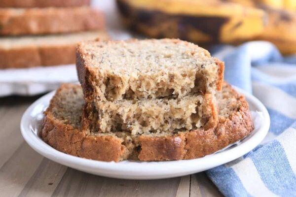 Two halves of banana bread on top of full slice on white plate