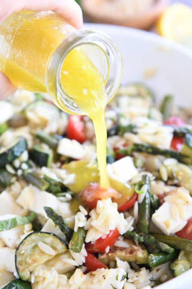 pouring lemon vinaigrette over orzo salad