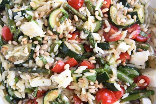close up view of orzo, pine nuts, zucchini, cherry tomatoes, asparagus, and fresh mozzarella