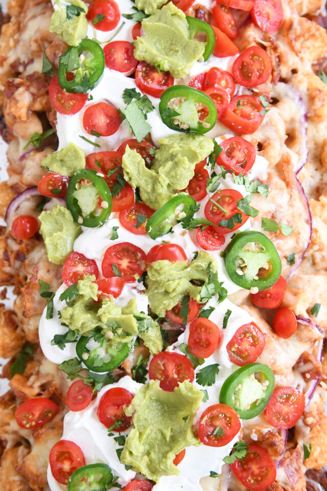 Close up top down view of bbq chicken totchos with sour cream, tomatoes and guacamole.