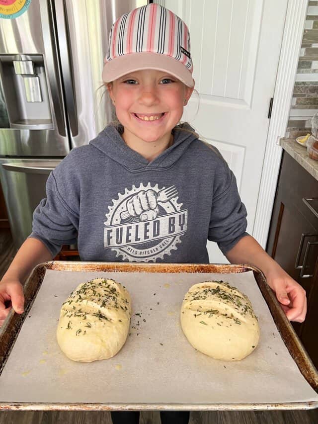 girl holding sheet pan with two loaves of bread