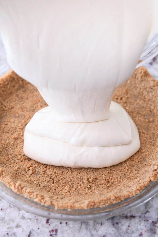 Pouring cheesecake batter into graham cracker crust.