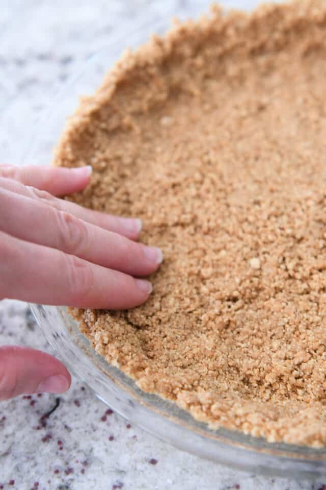 Pressing graham cracker crust into pie plate with fingers.
