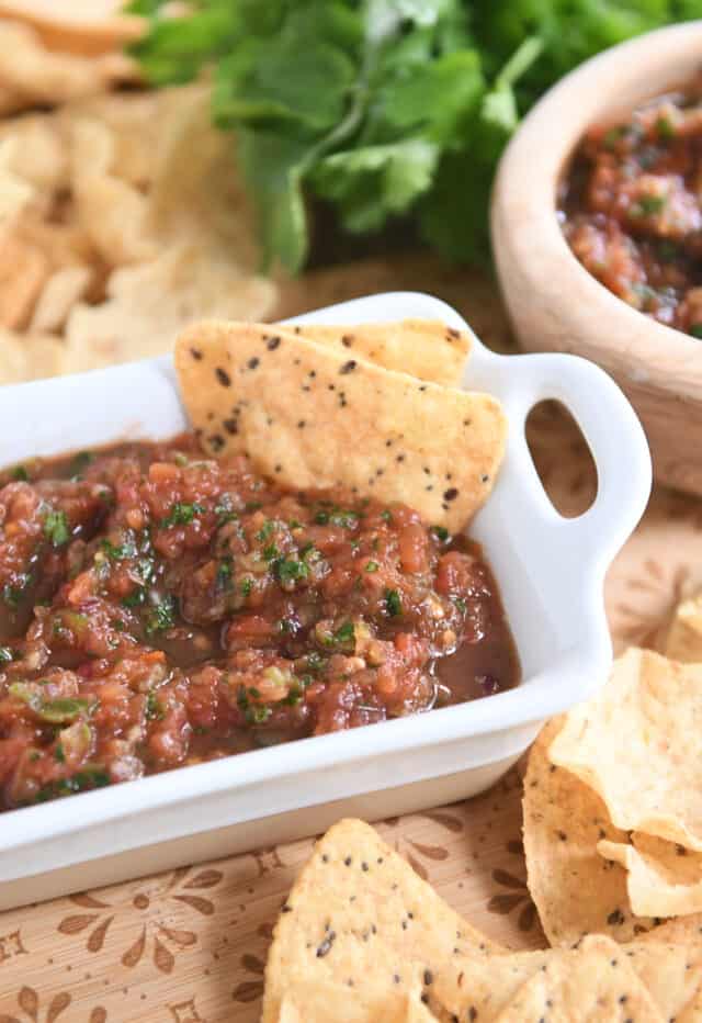 Homemade salsa in white dish with tortilla chips and cilantro in background.