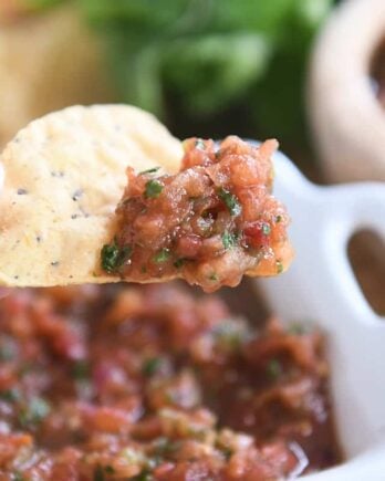 holding triangle tortilla chip with homemade salsa on tip of chip