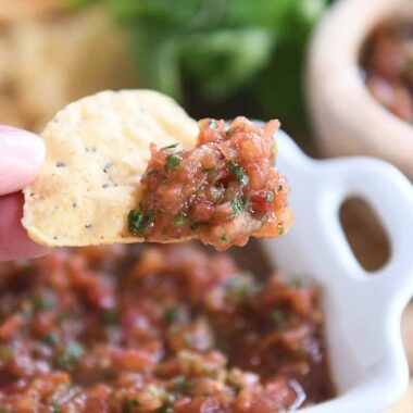 holding triangle tortilla chip with homemade salsa on tip of chip