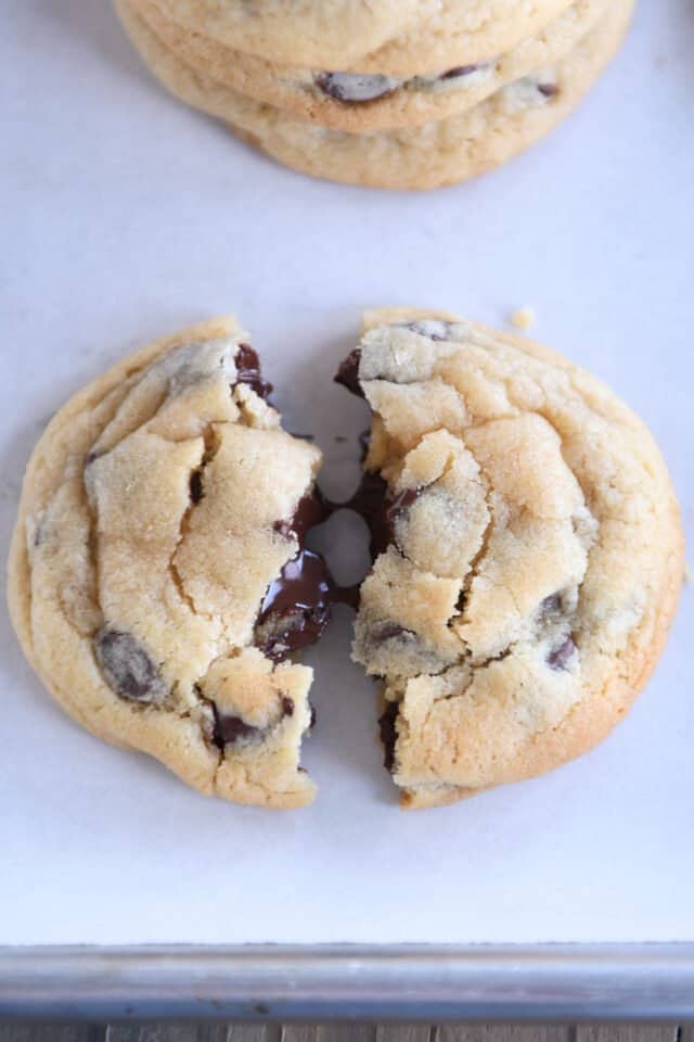 Super soft chocolate chip cookie broken in half on sheet pan.