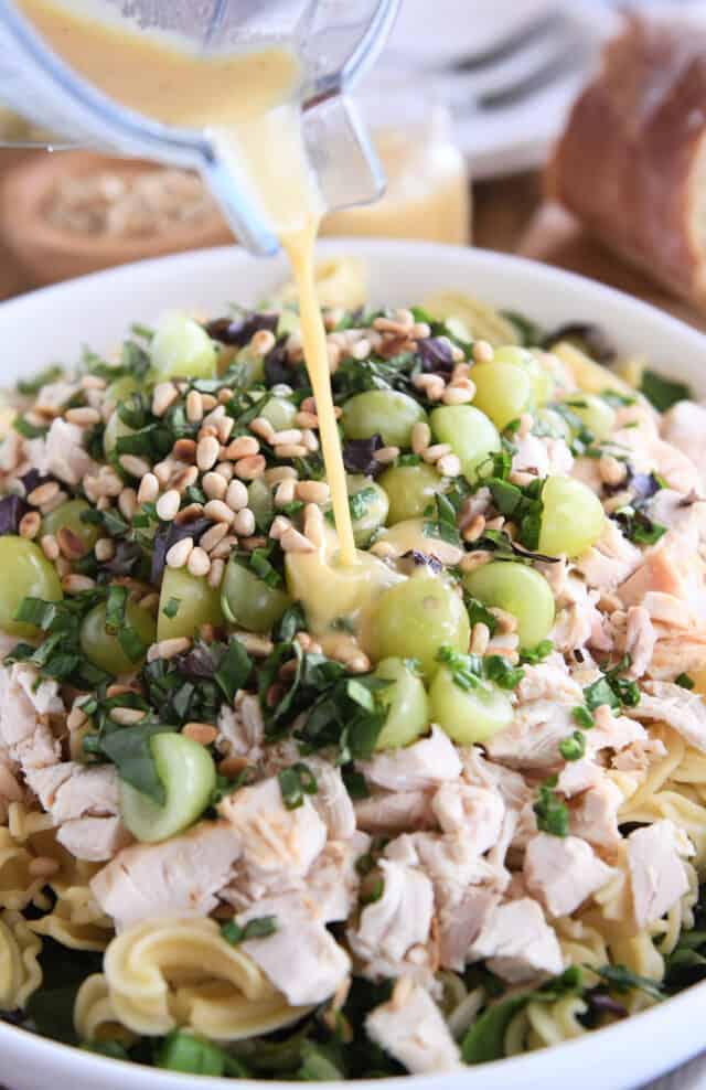 Pouring vinaigrette over grapes, greens, chicken, and pine nuts.