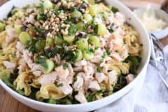 large white bowl with greens, pasta, chicken, grapes, fresh basil, and pine nuts