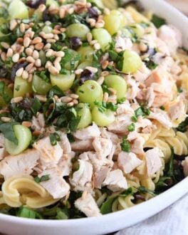 large white bowl with greens, pasta, chicken, grapes, fresh basil, and pine nuts