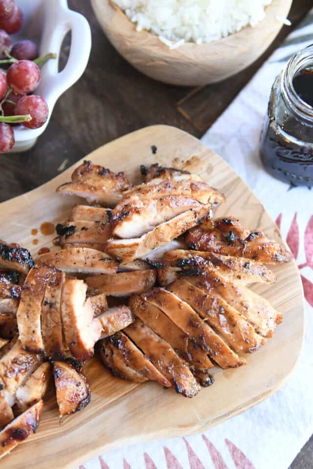 Slices of grilled teriyaki chicken on wood cutting board.