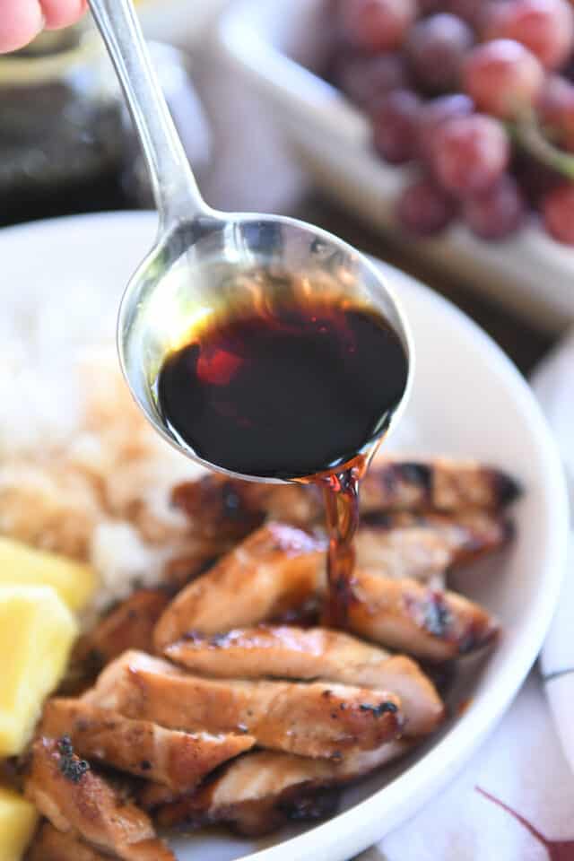 Drizzling teriyaki sauce over slices of chicken in white bowl.