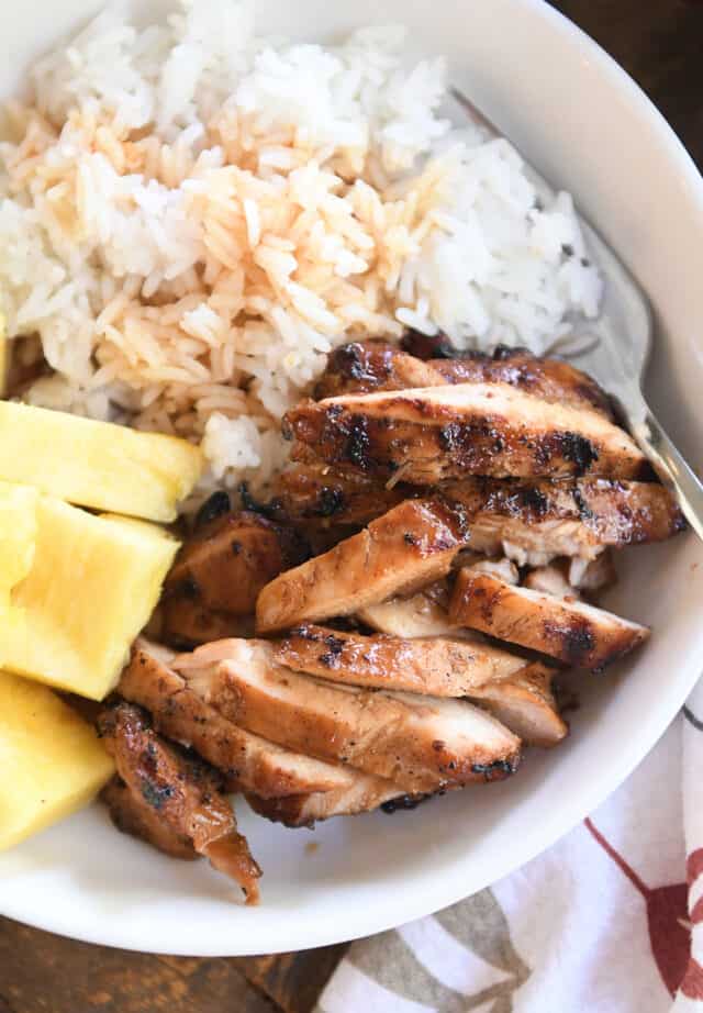 Slices of grilled teriyaki chicken in white bowl with rice and pineapple.