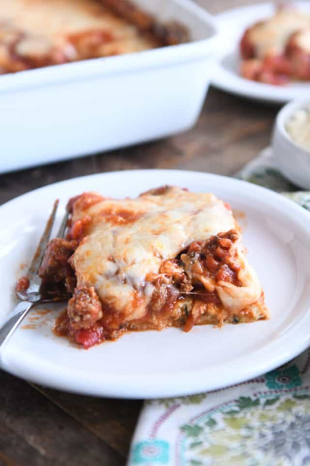Square of zucchini spaghetti casserole on white plate with fork.