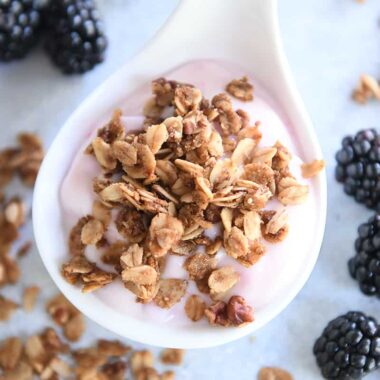 White scoop with strawberry yogurt, cinnamon granola and blackberries on the side.