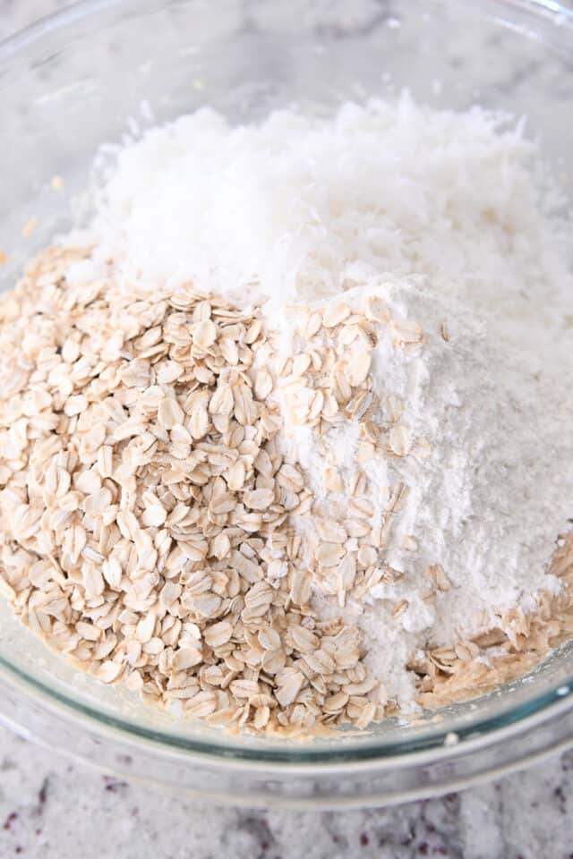 Oats, flour, and coconut in bowl with cookie dough.