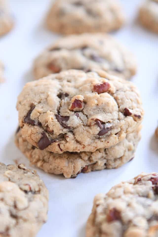 Two cowboy cookies stacked on white parchment paper.