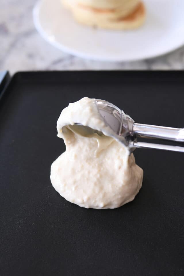 Portioning pancake batter onto hot griddle with large cookie scoop.