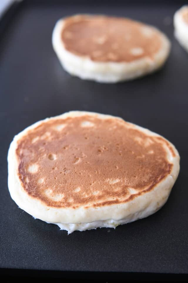 Two golden baked pancakes on hot griddle.