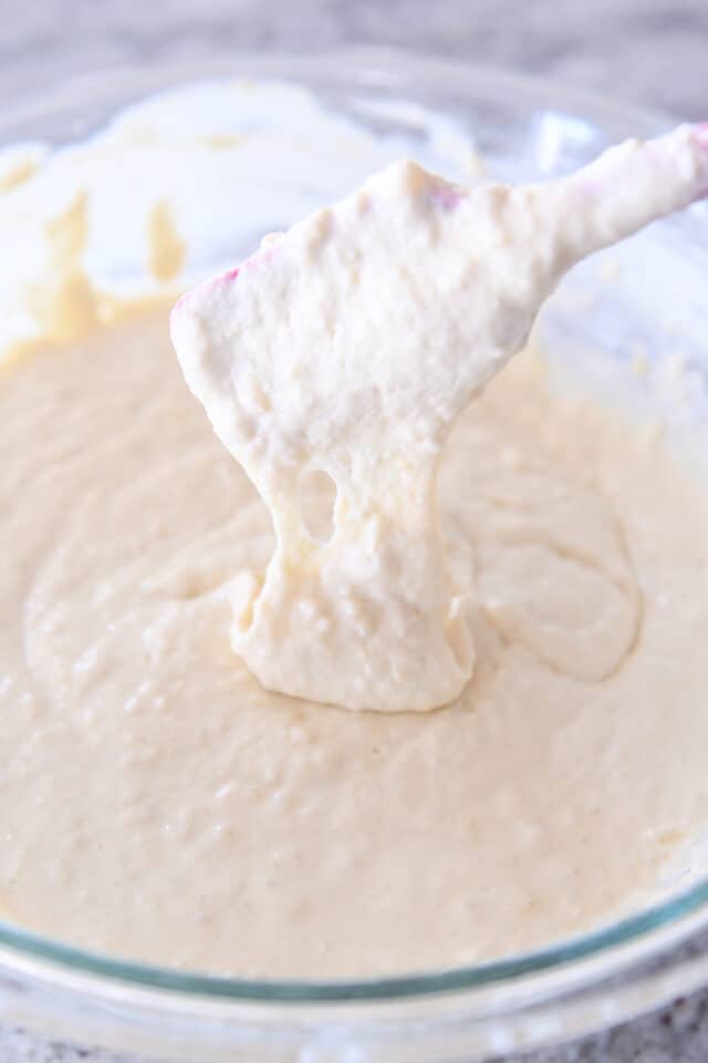 Rubber spatula lifting up pancake batter with batter dripping off into bowl.