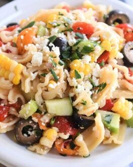 Serving of Greek pasta salad on white plate with fork to the side.