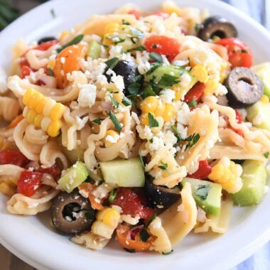 Serving of Greek pasta salad on white plate with fork to the side.