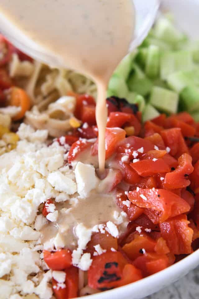 Pouring vinaigrette dressing over red peppers and feta cheese.