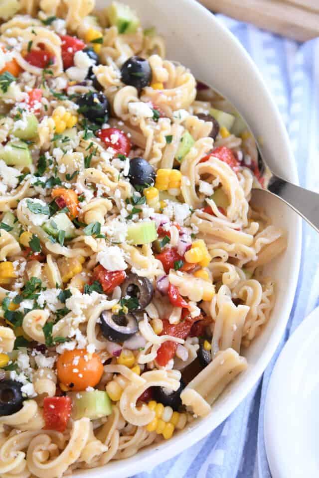 Greek pasta salad in large white serving bowl with serving spoon.