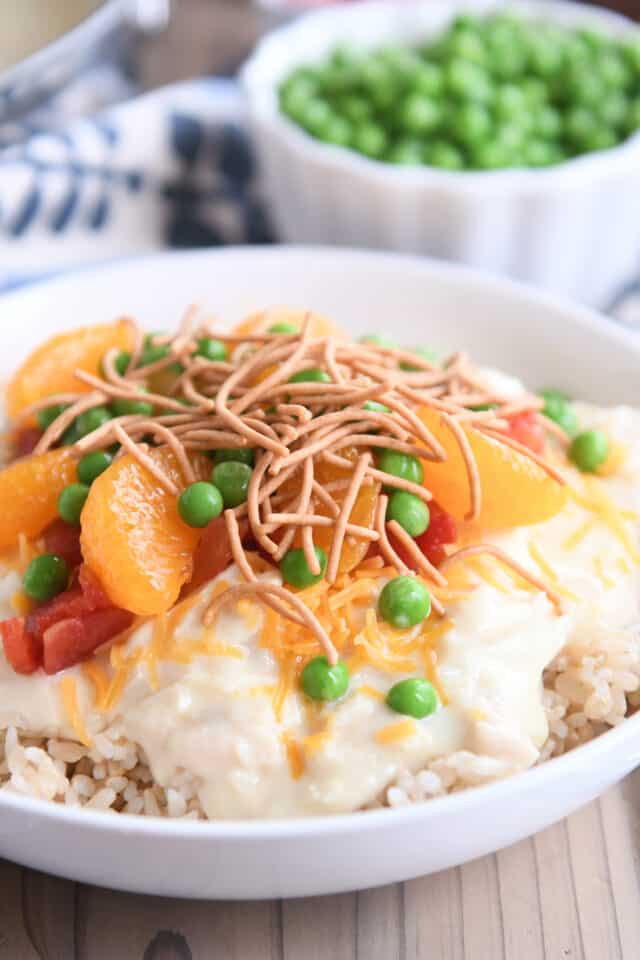 White bowl with rice, chicken gravy, peas, cheese, mandarin oranges and peas.
