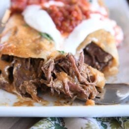 Two enchiladas on white plate with bite of enchilada on fork.