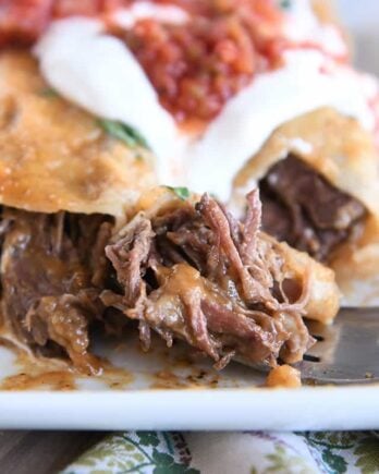 Two enchiladas on white plate with bite of enchilada on fork.