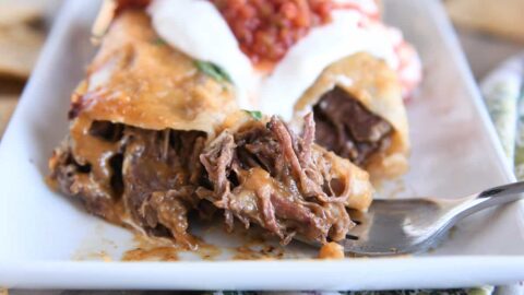 Two enchiladas on white plate with bite of enchilada on fork.