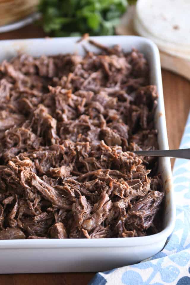 Shredded Mexican beef in white pan with fork.