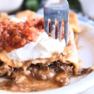 Saucy Mexican beef enchiladas on white plate with sour cream and salsa.