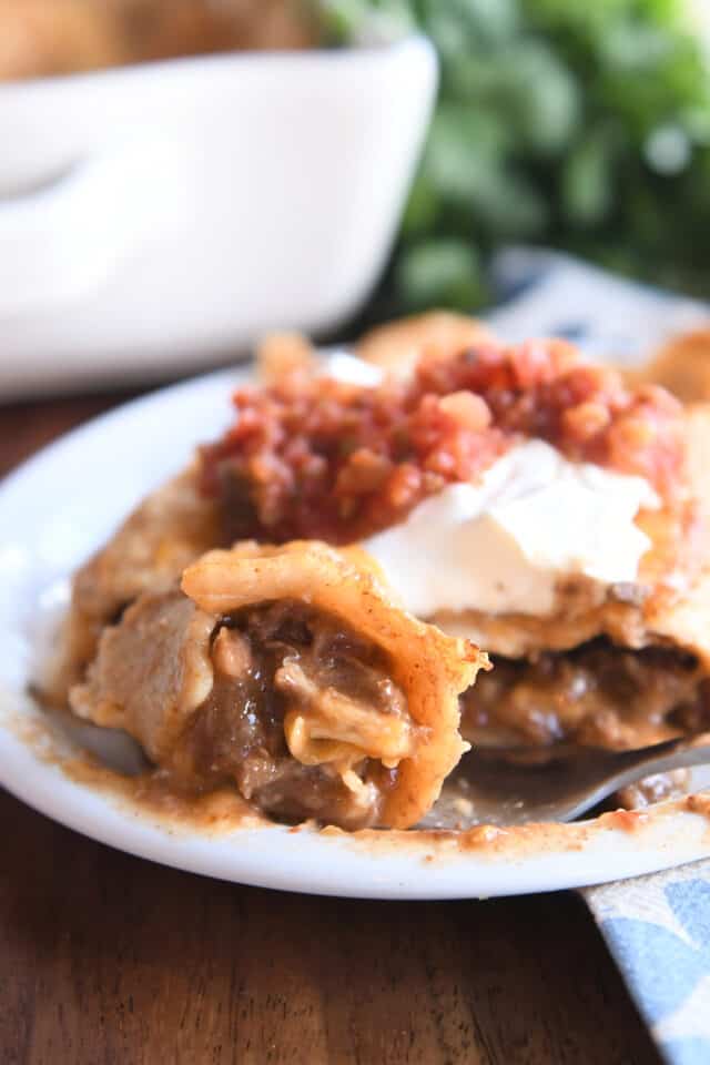 Bite of saucy enchilada on white plate with fork.
