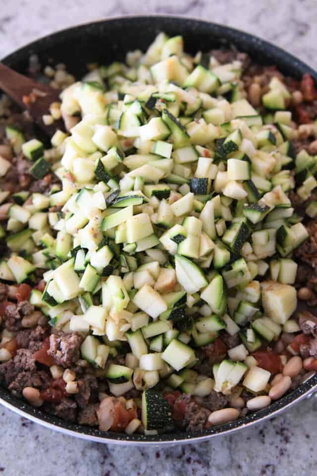 Finely chopped zucchini on top of ingredients in skillet.