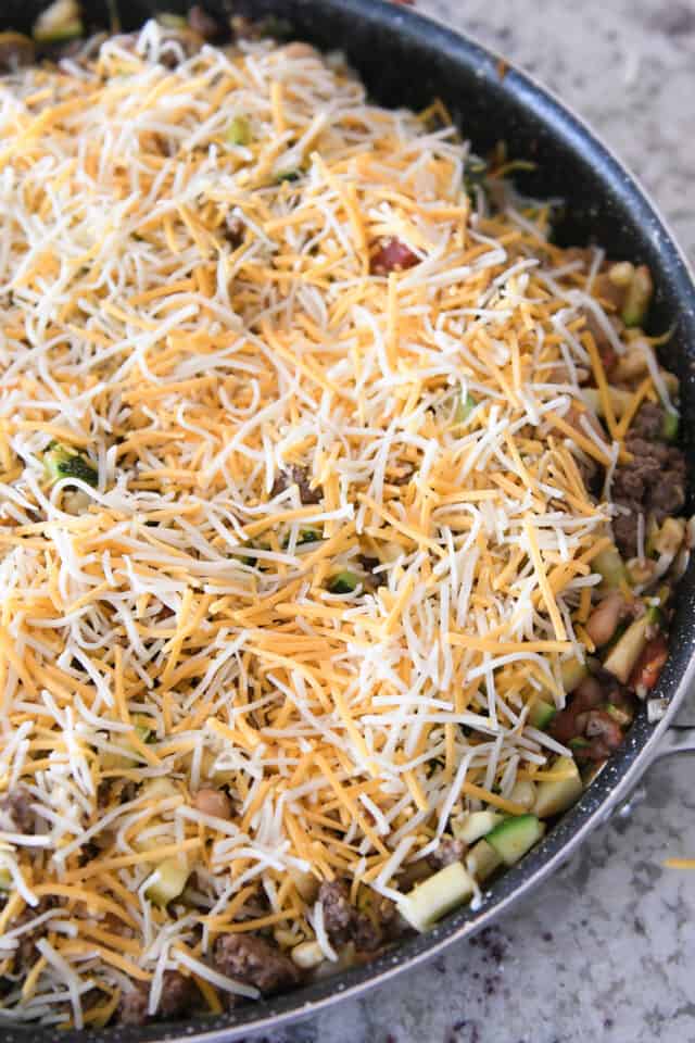 Shredded cheese covering ingredients in skillet.