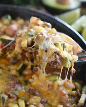 serving spoon lifting up cheesy portion of zucchini skillet