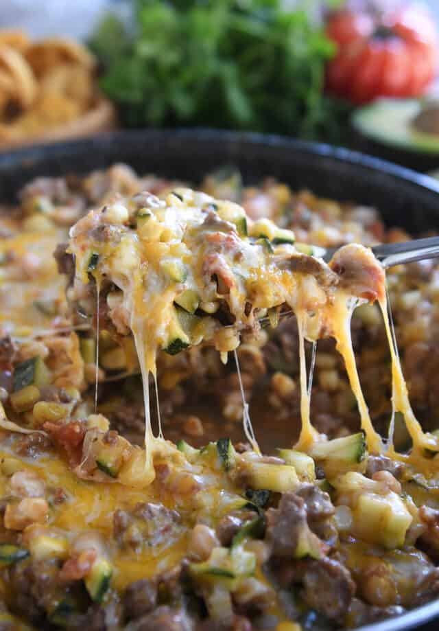 Serving spoon lifting up cheesy portion of zucchini skillet.