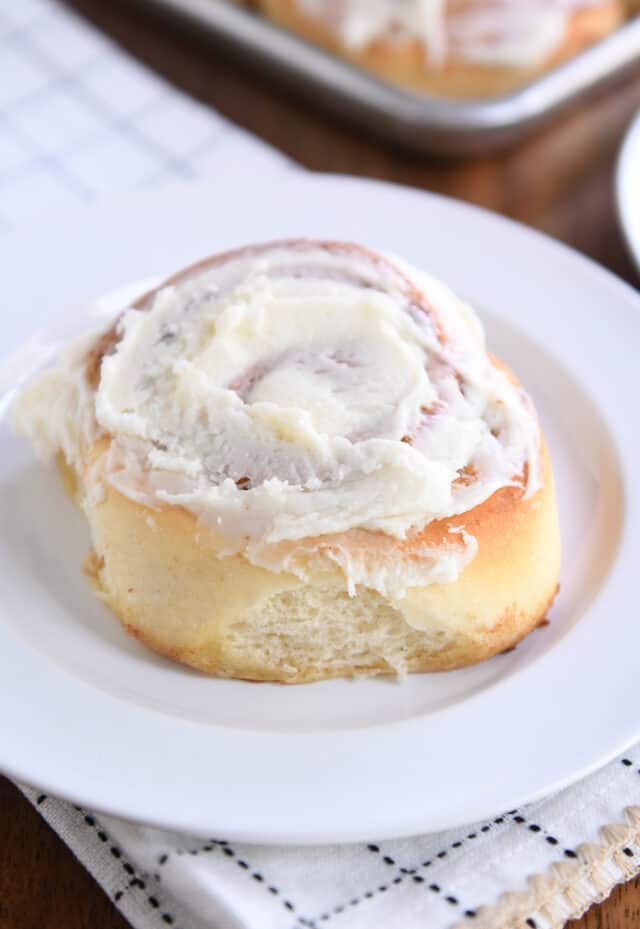 Fluffy frosted cinnamon roll on white plate.