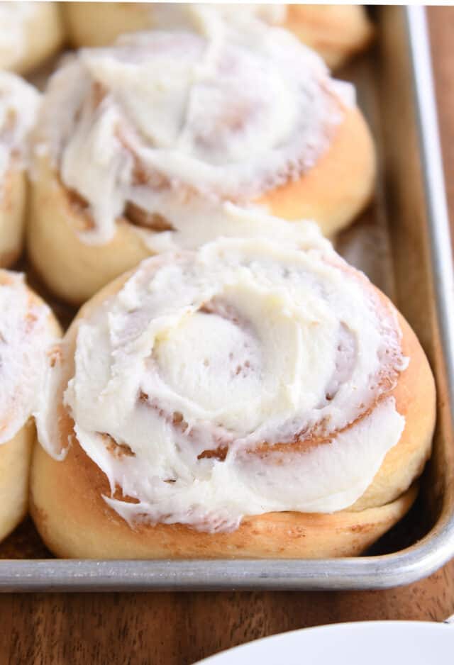 Baked cinnamon rolls on sheet pan with frosting.