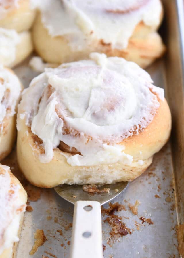 Spatula underneath baked cinnamon roll on sheet pan.