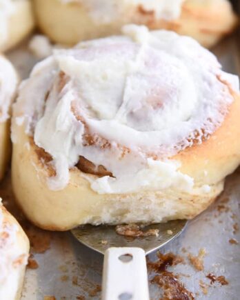 spatula lifting up baked frosted cinnamon roll on sheet pan