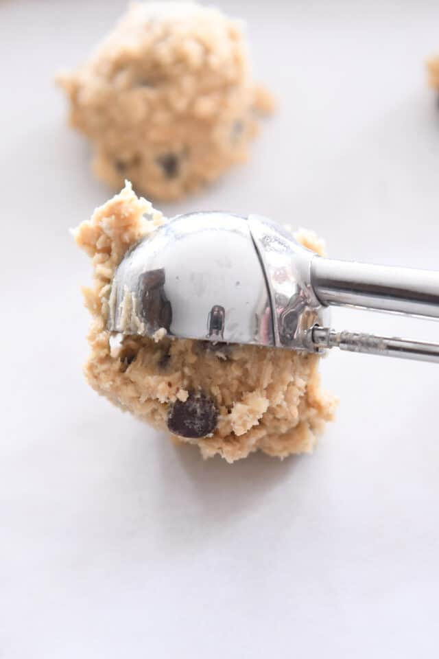 Cookie scoop scooping out cookie dough ball onto parchment-lined baking sheet.